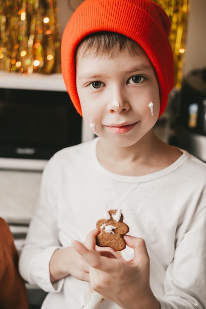 Photo boy decorate christmas cookies with white icing. children decorate a gingerbread man on a wooden background. christmas sweets with cocoa and marshmallows for children.