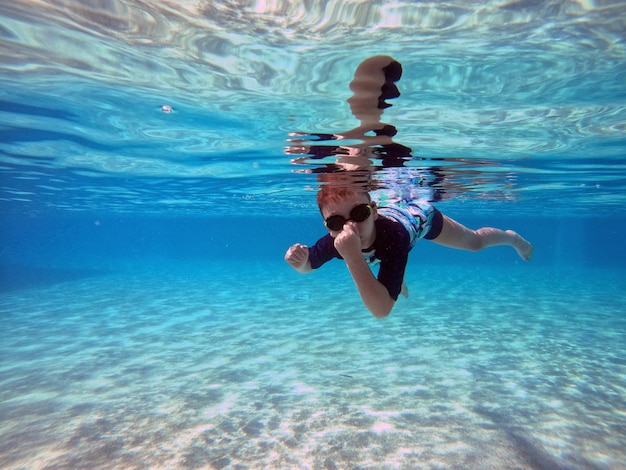 少年は澄んだ青い水のプールで水中に飛び込みます