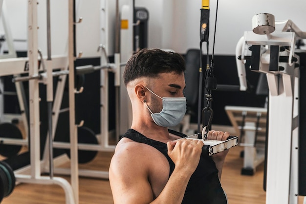 Photo boy doing exercise with the gym pulley with mask