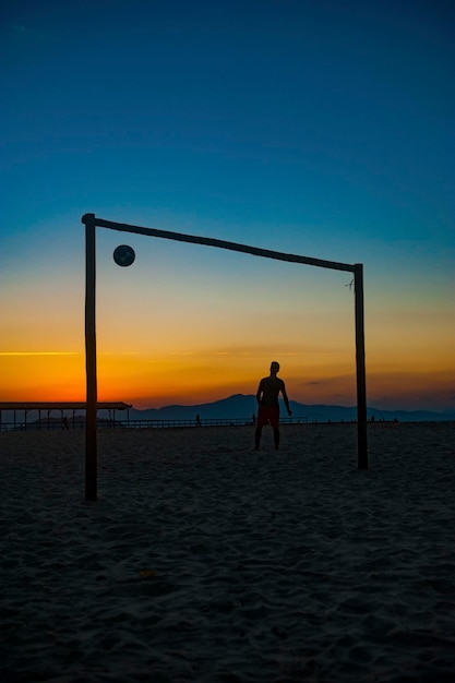 Boy doing sports with ball on the beach in full summer sunset on the Brazilian coast