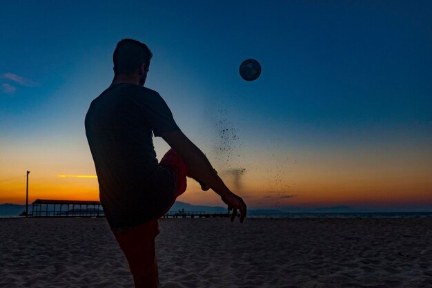 브라질 해안의 완전한 여름 일몰에 해변에서 공을 가지고 스포츠를 하는 소년