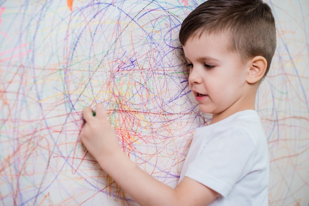 少年は色のチョークで壁に描画します。子供は家で創造性に従事しています