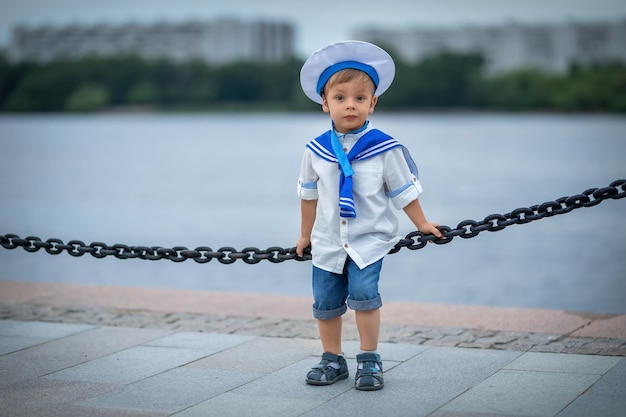 A boy dressed as a sailor stands on the pier looks at the ships and dreams