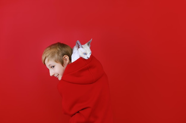 Boy dressed in a red tracksuit with a cat on his shoulders on a red background