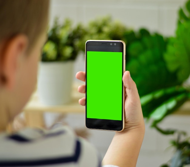 Photo the boy dressed in a striped longsleeve sits and is holding a phone in his hand