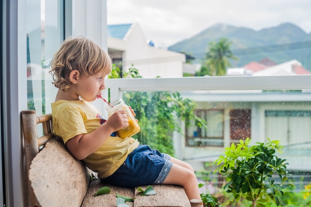 Boy drinking juicy smoothie from mango in glass mason jar with striped red straw