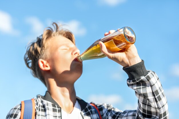 写真 美しい青い空の背景でボトルからレモネードを飲んでいる少年