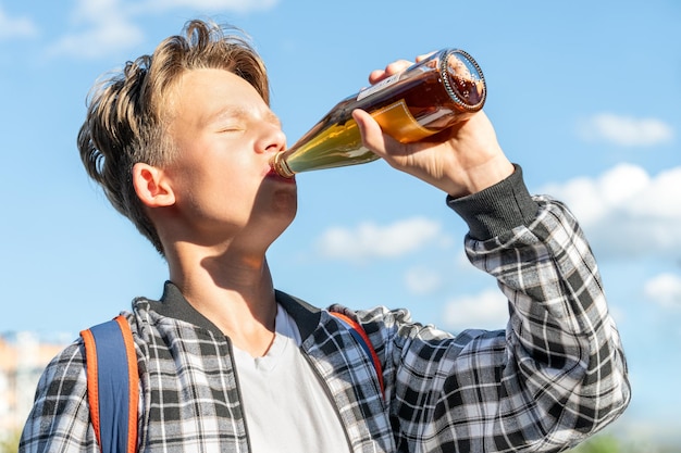 写真 美しい青い空の背景でボトルからレモネードを飲んでいる少年