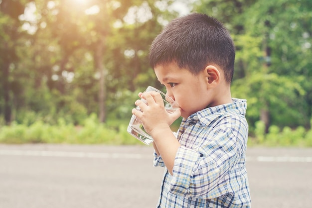 Boy drinking water from glass while standing on road against trees