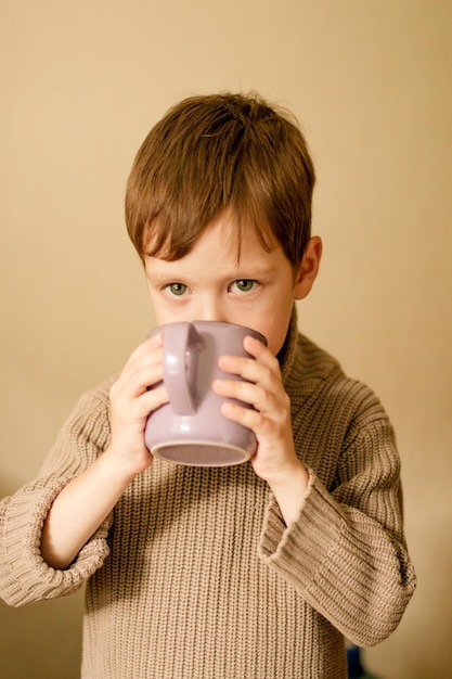 茶色のスウェットを着た男の子がカップから飲む