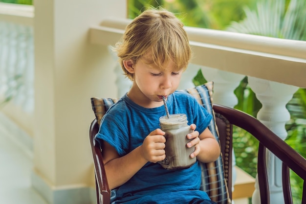 A boy drinks a drink from a carob