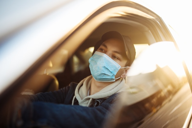 A boy drives a car in a medical sterile mask during coronavirus pandemic quarantine