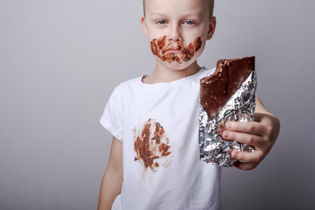 Ragazzo che mangia una tavoletta di cioccolato nel suo sorriso e vestiti imbrattati