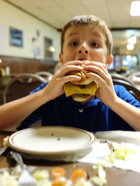 Photo boy eating cheeseburger at restaurant