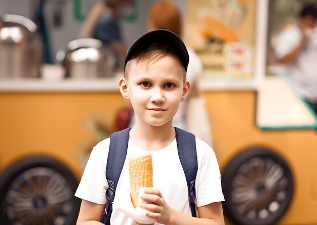 ストリートマーケットのフードトラックで新鮮なゆでトウモロコシを食べる少年。