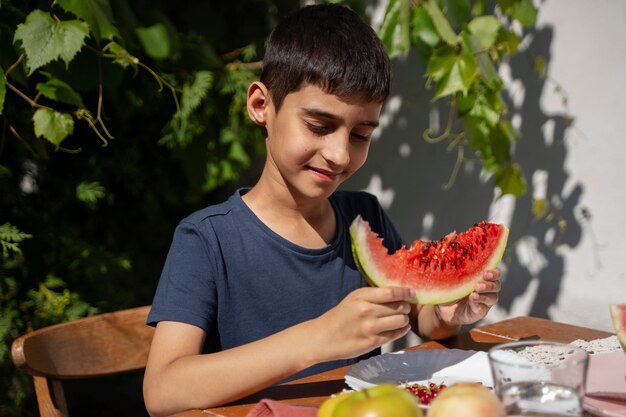 屋外のテーブルでスイカを食べる少年