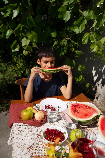 Boy eating watermelon outdoors at table