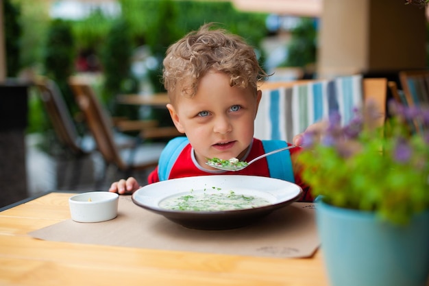 The boy eats in a cafe The boy on the summer terrace eats okroshka