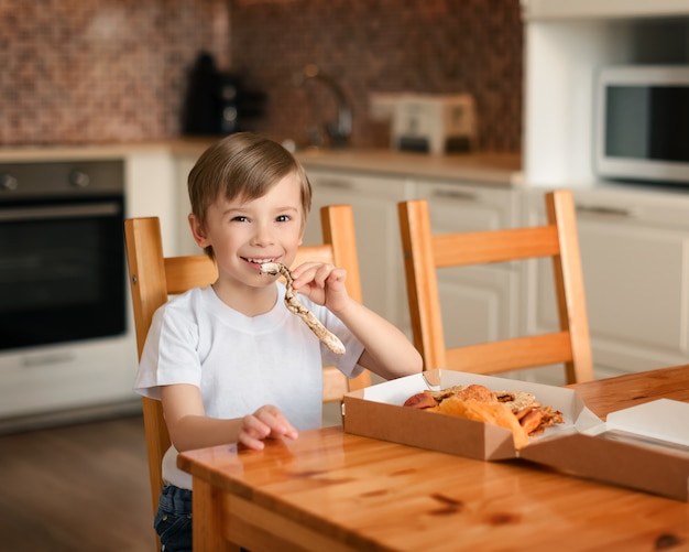 The boy eats a dried banana in the kitchen