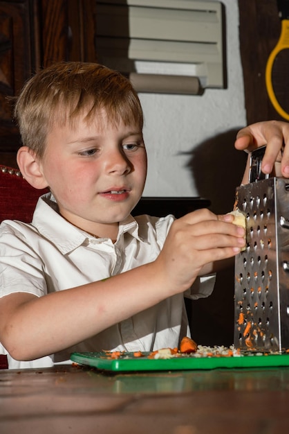 A boy of eight prepares a salad rubs on a grater and cuts real photo