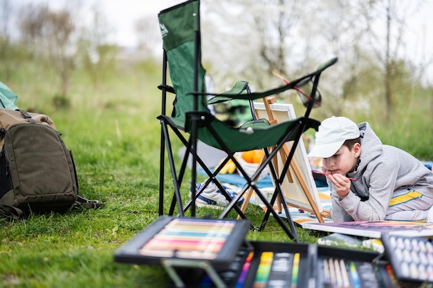 Boy enjoying outdoor on picnic blanket and painting on canvas at garden spring park relaxation