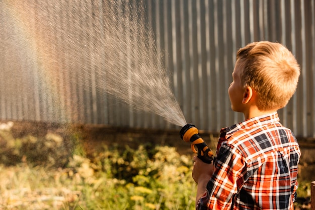 男の子は庭で水やりをしながら虹を楽しんでいます