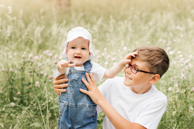 Photo boy in eyerglasses with baby sister in an outdoor setting