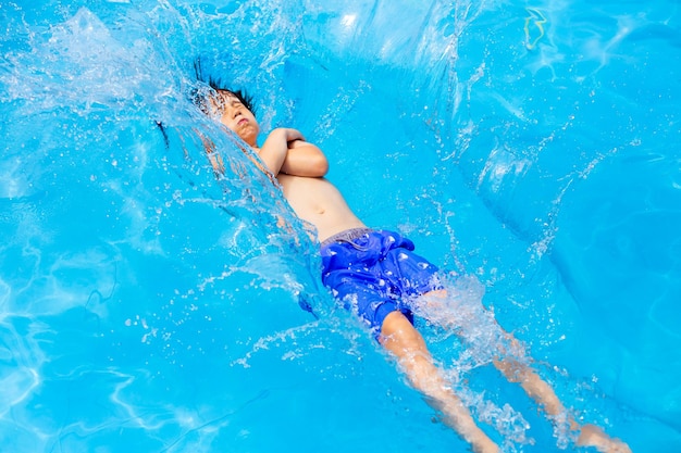 Boy falls into the pool to cool off Teenager refreshing in summer heat jumping in the swimming pool Holidays concept