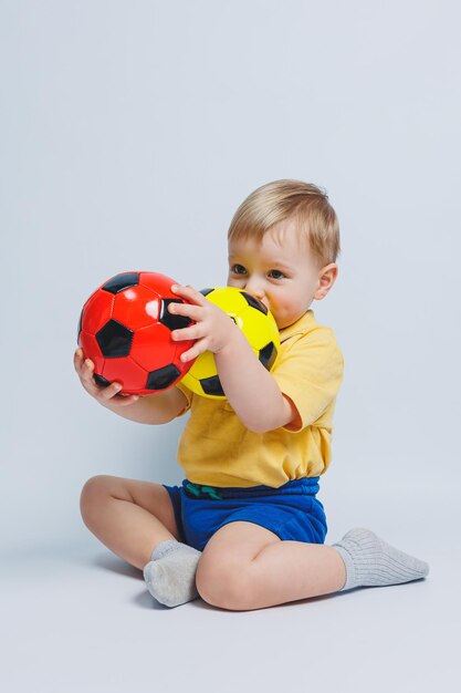 Boy fan holding a soccer ball in his hands isolated on a white background newbie child in football sport for kids Little athlete Yellow and blue football kit for kids