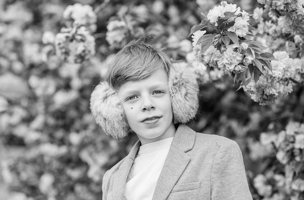 Boy fashionable teen posing near sakura Confident stylish child enjoy warm spring day Sakura garden concept Child pink flowers of sakura tree background Guy enjoying cherry blossom sakura