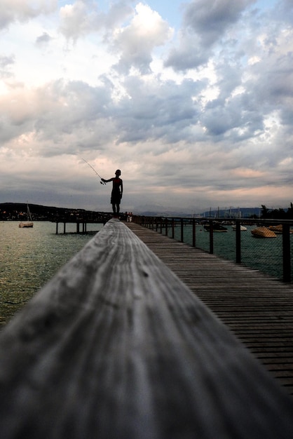 Photo boy fishing while standing on jetty by boats and river