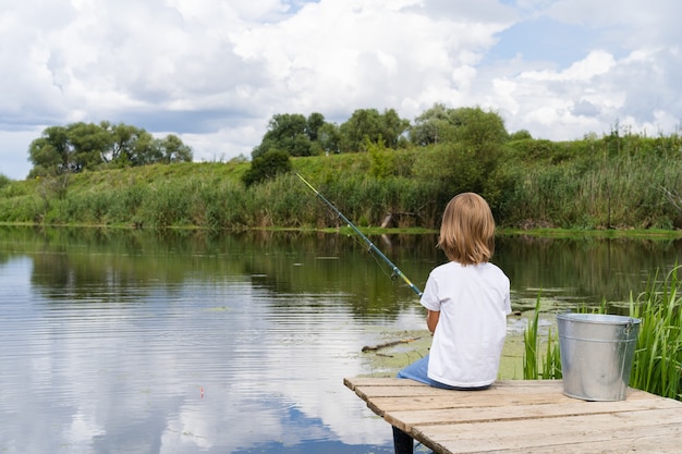 Photo boy fishing on a wooden bridge near a pond