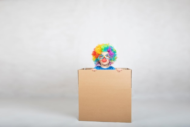 Boy of five years dressed in the costume of a clown stays in a carton paper box. Closeup