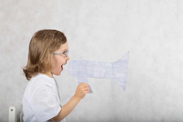 Boy of five years is announcing something at loudspeaker. Gray background.