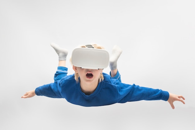Boy flies in virtual reality glasses. White surface. Virtual reality games.
