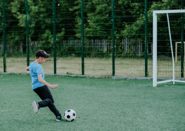 the boy on the football field kicks the ball the boy runs on the green lawn for the ball