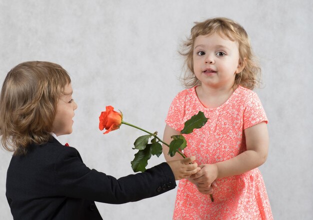 Boy of four years is presenting a rose to the girl