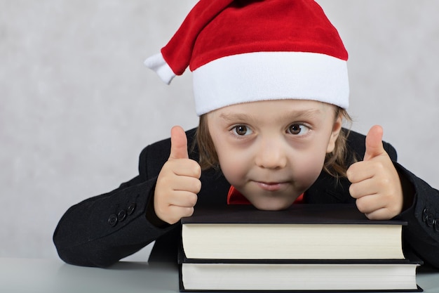 Boy of four years in Santa's hat close to books. Closeup