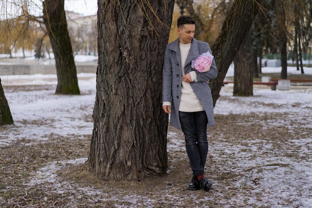 Boy friend with a bouquet of pink flowers hydrangea waiting for his girl friend outdoors while snow is falling. Valetnine`s day concept, wedding proposal. 
man goes on a date.