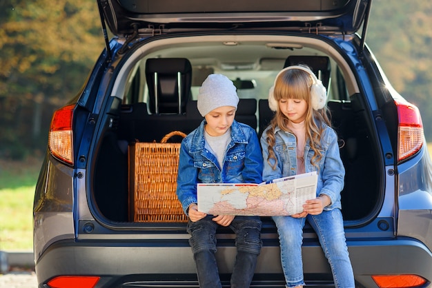 boy and girl are looking at the road map while sitting in the auto's trunk