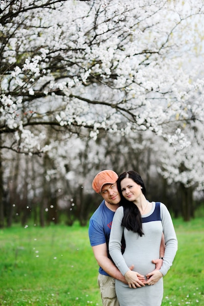 Boy and girl on the of blossoming apricot. A guy hugs a pregnant woman