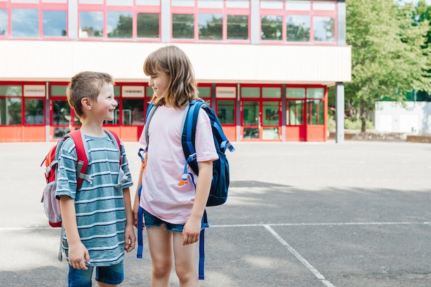 Foto un ragazzo e una ragazza, un fratello e una sorella, stanno con gli zaini sulla schiena davanti alla scuola.