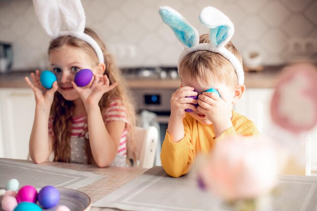 Photo boy and girl in bunny ears at breakfast on easter morning at table with easter eggs basket kids celebrating easter children on easter egg hunt home decoration cozy having fun