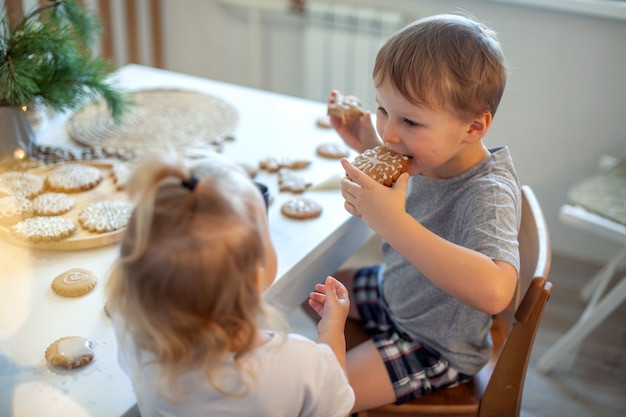 男の子と女の子が家でクリスマスのジンジャーブレッドを飾って食べています男の子と女の子はコルネットでペイントしています...