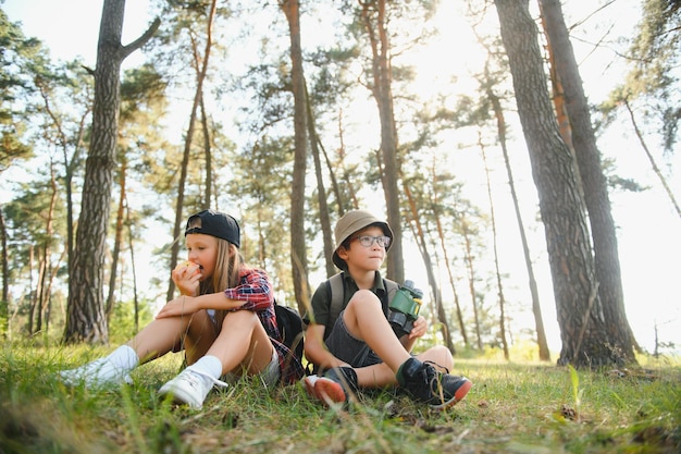 Photo boy and girl go hiking with backpacks on forest road bright sunny day