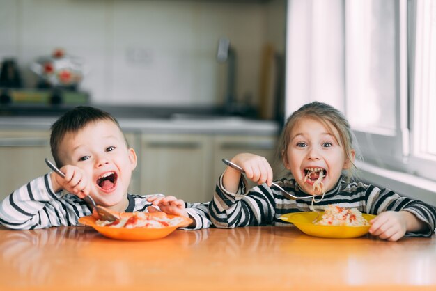Мальчик и девочка на кухне едят пасту и кричат от удовольствия