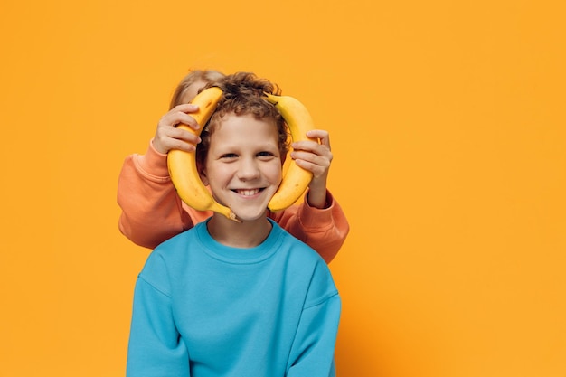 Boy and girl playing with bananas against yellow background