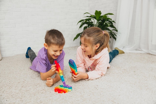 Boy and girl sitting on the floor and playing with silicone toy, antistress. Pop is a sensory toy. Relieve stress.