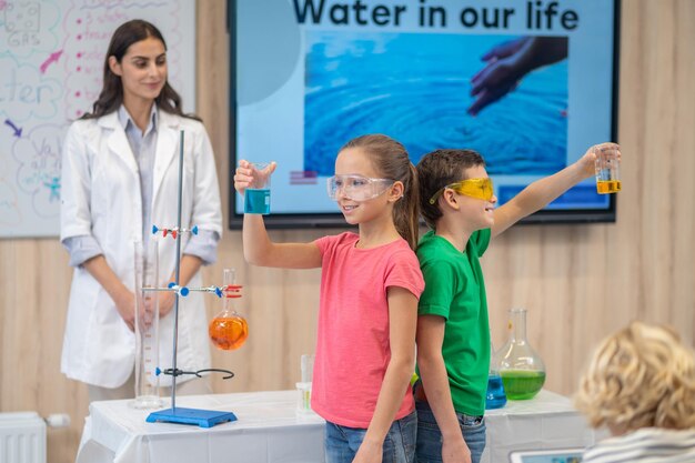 Boy and girl standing back to back holding beakers