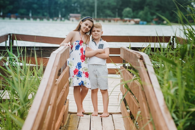 Boy and girl standing on a wooden pier on a lake shore. Summer vacation